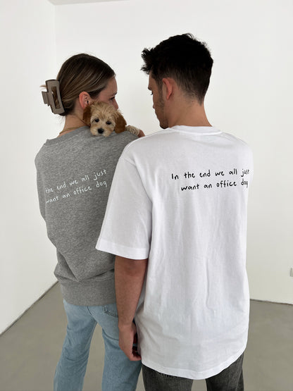 office dog shirt, getragen von einer männlichen Person, rückenansicht, weiß mit schwarzem Schriftzug "in the end we all just want an office dog", unisex, rückenansicht. grauer office dog sweater mit selbem print, getragen von einer weiblichen person mit hund auf der Schulter.